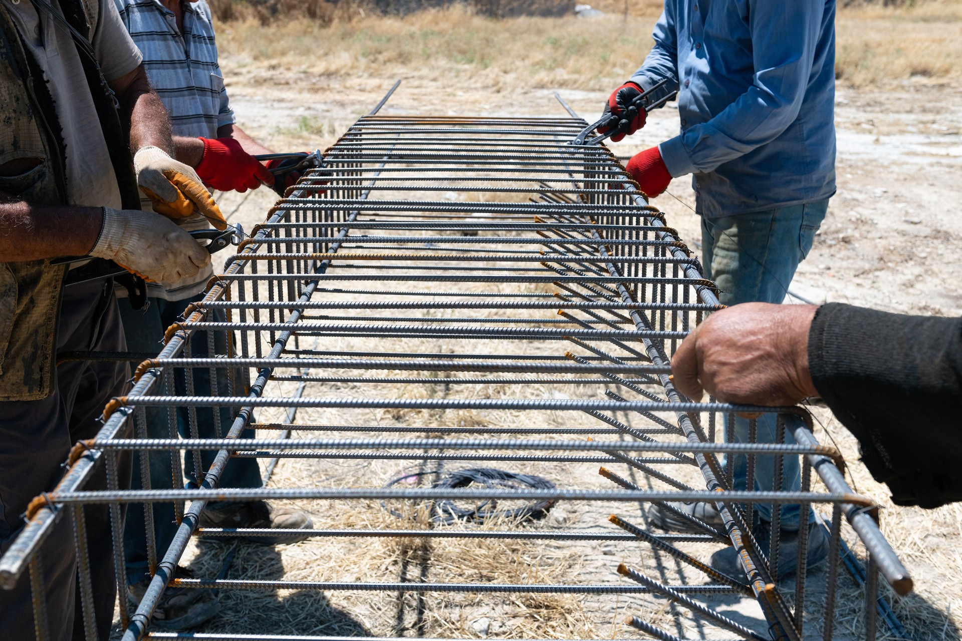 Workers use steel lacing wire to attach steel bars to reinforcing bars. Close-up. Reinforced concrete structures - knitting a metal reinforcing cage